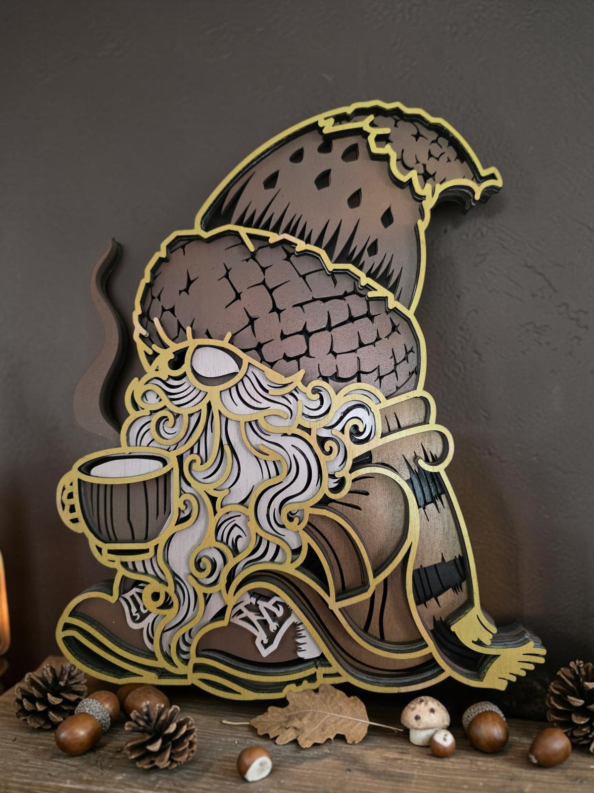 Cozy layered wooden fall gnome wall art holding a warm drink, styled with acorns, pinecones, mushrooms, and autumn decor