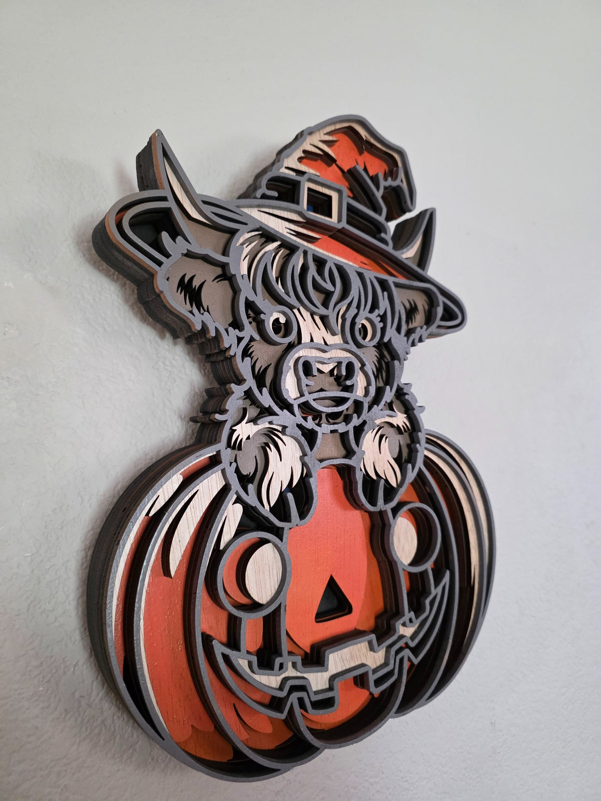 Side view of layered wooden Highland cow witch and jack-o-lantern wall art showing dimensional wood layers