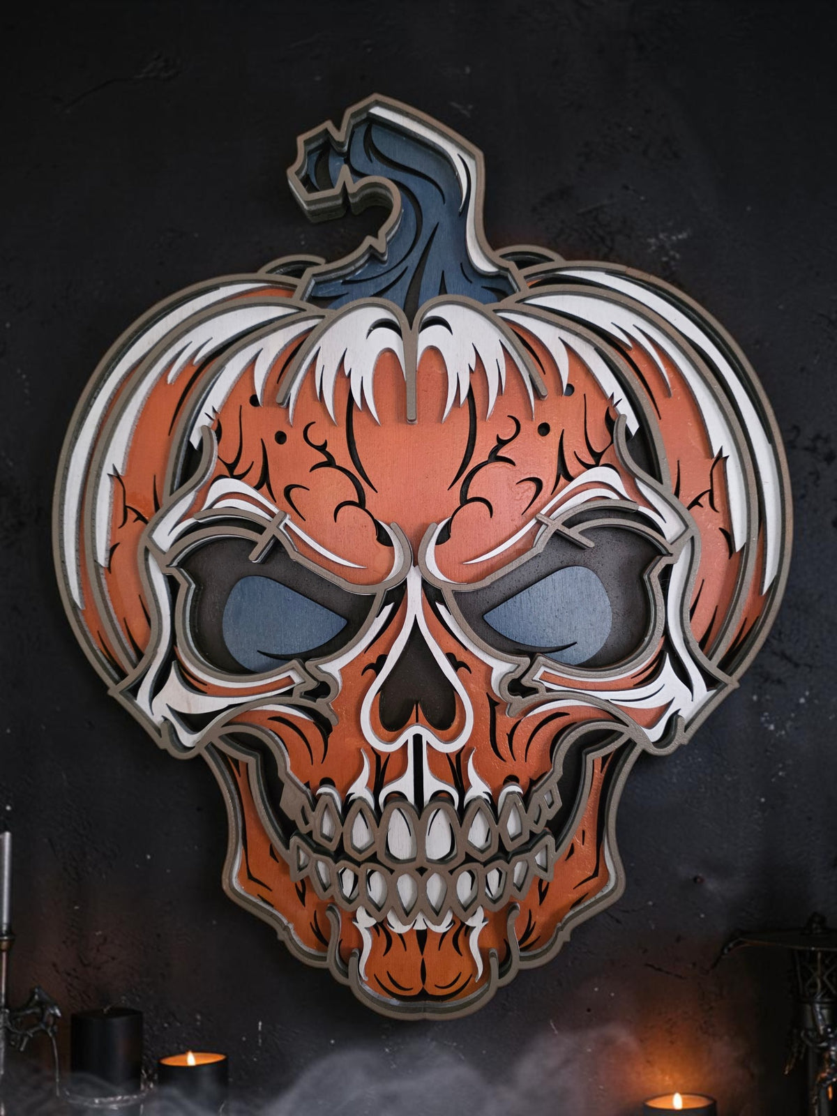 Layered wooden pumpkin skull Halloween wall art styled on a dark spooky wall with candles and fog