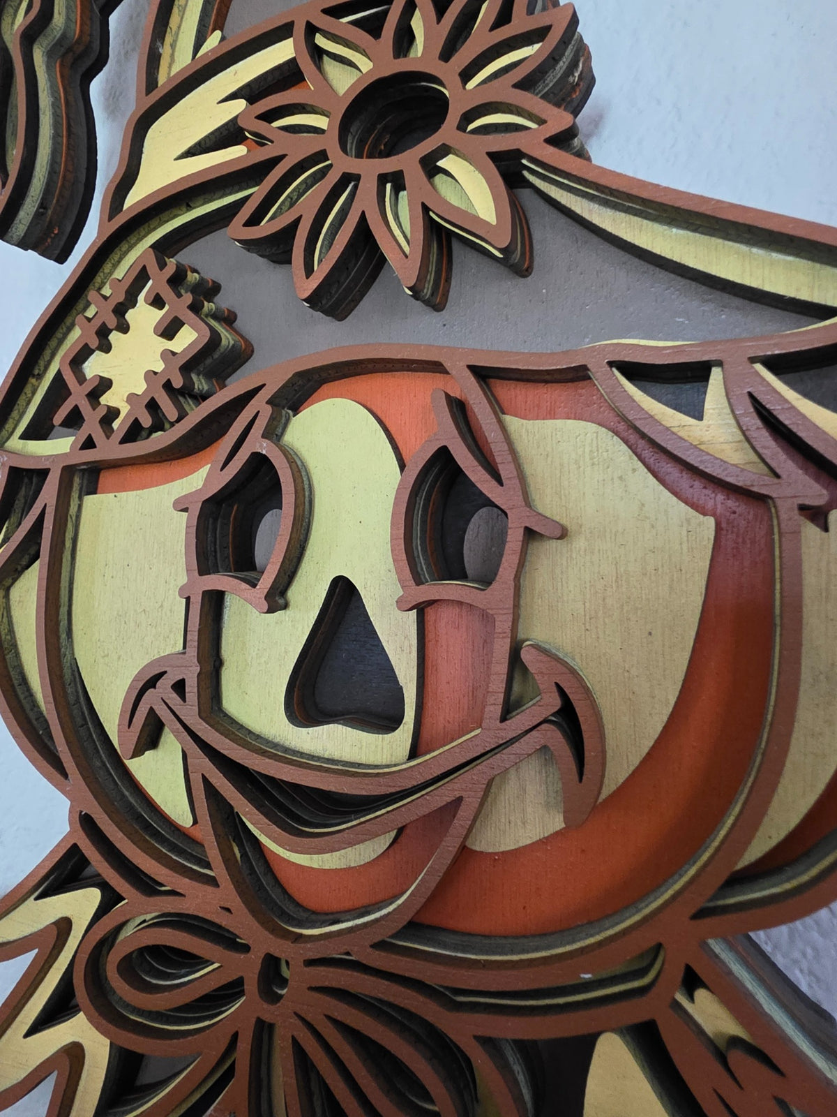 Close-up detail of smiling pumpkin scarecrow face and layered wood construction