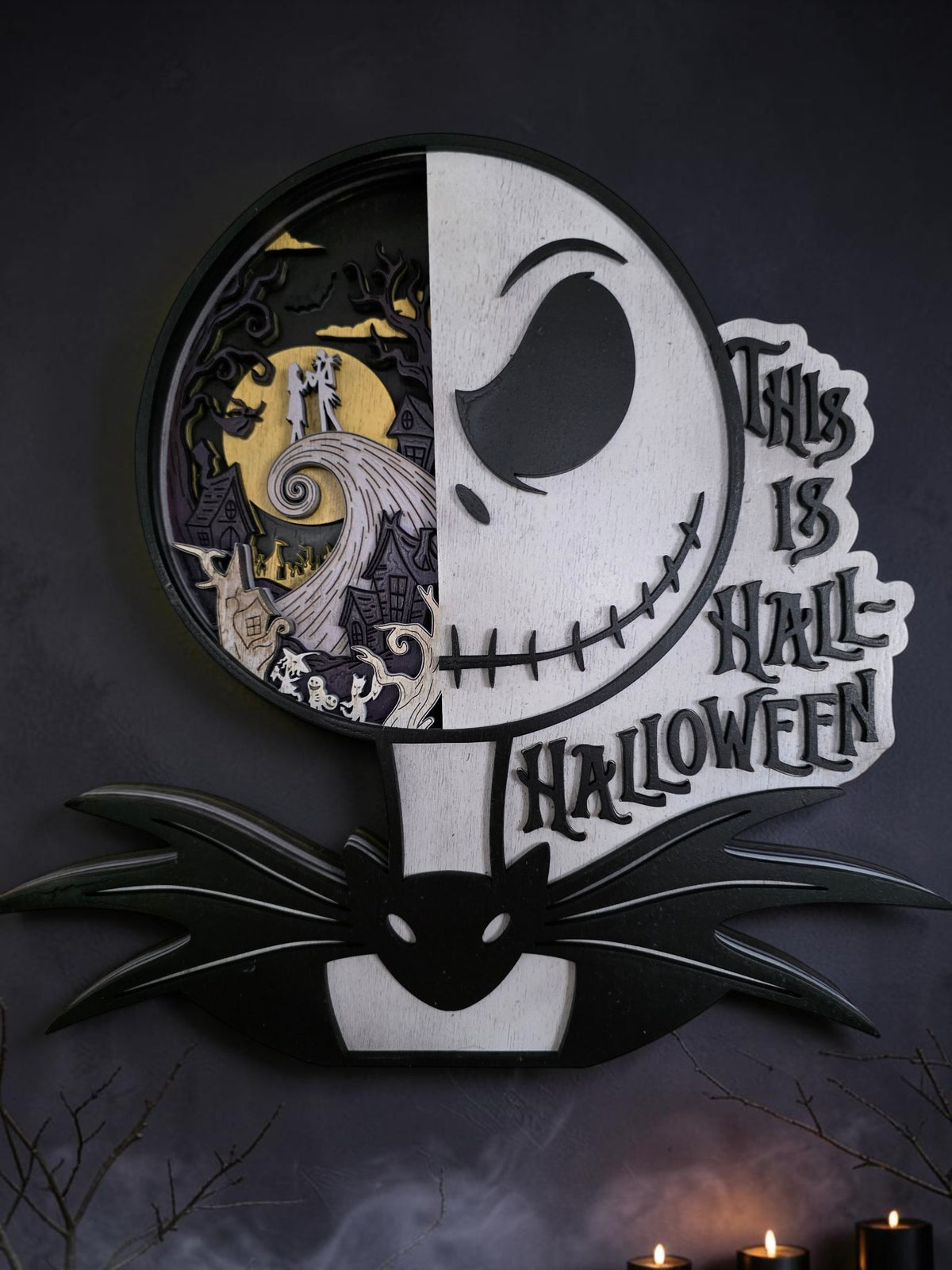 Layered wooden This Is Halloween split-face wall art with a moonlit spooky town scene, styled on a dark wall with candles and fog